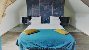 Un dormitorio con techo inclinado, una cama con colcha azul y amarilla, dos almohadas y cabecero de madera con diseño de olas.