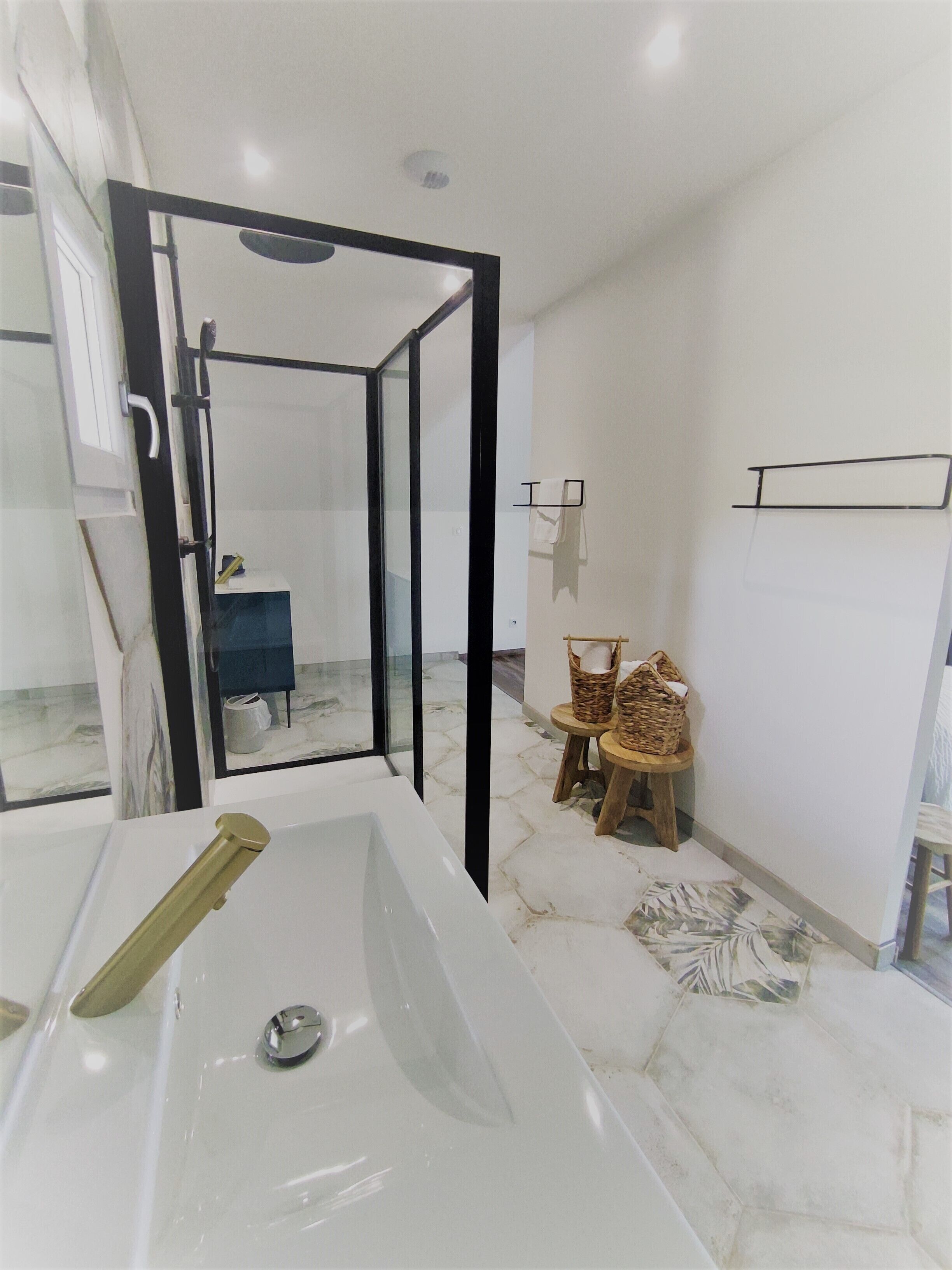 A modern bathroom with a large bathtub, a glass shower enclosure, and a small seating area with baskets.