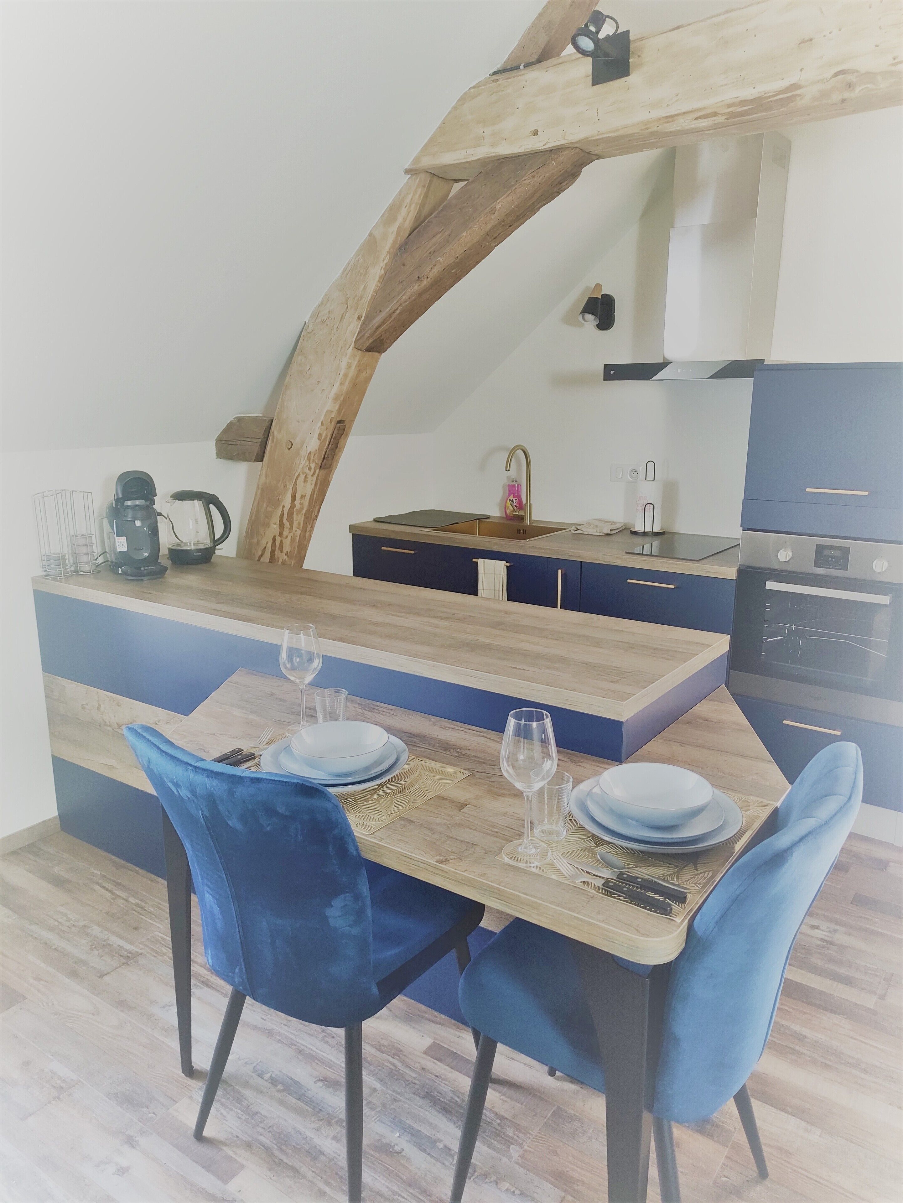 Un comedor con una mesa de madera, sillas azules y una cocina al fondo.
