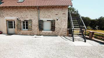 Een gebouw van steen met een dak van rode tegels, een oprit van grind en een metalen trap die leidt naar een houten terras.