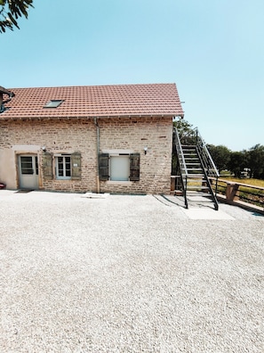 Ein Steinhaus mit rotem Ziegeldach, einer Schotterauffahrt und einer Metalltreppe, die zu einem Holzbalkon führt.