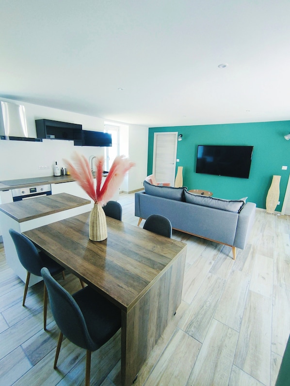 Eine moderne Küche mit Essbereich, einem grauen Sofa und einem Flachbildfernseher an einer türkisblauen Wand.