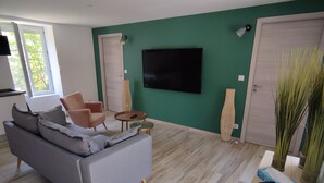 Una sala de estar moderna con un sofá gris, una mesa de centro de madera y un televisor de pantalla plana montado en una pared verde.