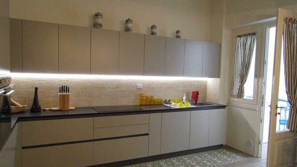 A modern kitchen with light-colored cabinets, a black countertop, and a patterned rug. - Apartment in the historic center (Camaiore)