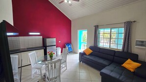 Un espacio habitable compacto con kitchenette, un comedor con mesa de vidrio y un sofá con cojines.