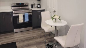 Une cuisine moderne avec des meubles blancs, un four à micro-ondes, un four et un mixeur. On y trouve une table ronde avec deux chaises blanches et un vase de fleurs.
