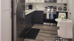 Une cuisine moderne avec des meubles blancs, des appareils en acier inoxydable et un petit coin repas comprenant une chaise et une table blanches.