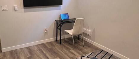 Una sala de estar moderna con una televisión de pantalla plana montada en la pared, una computadora portátil sobre una mesita, una silla blanca y una mesa de centro con un jarrón de flores.
