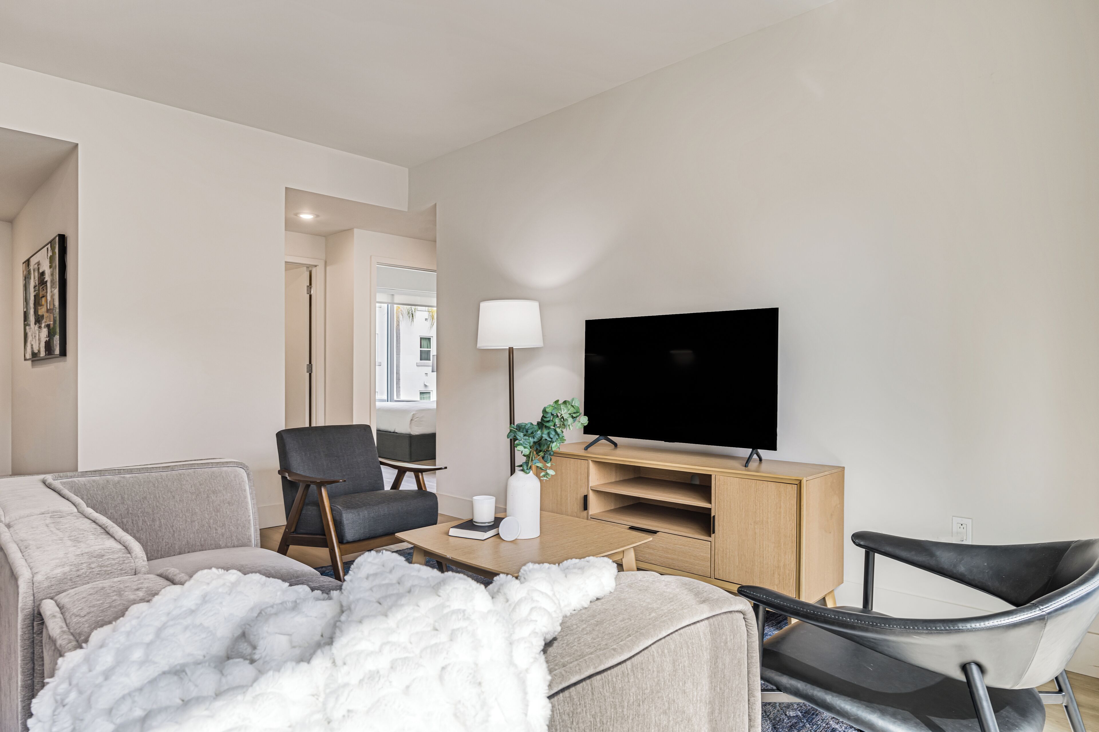 A modern living room with a sofa, armchair, coffee table, TV stand, and a lamp.