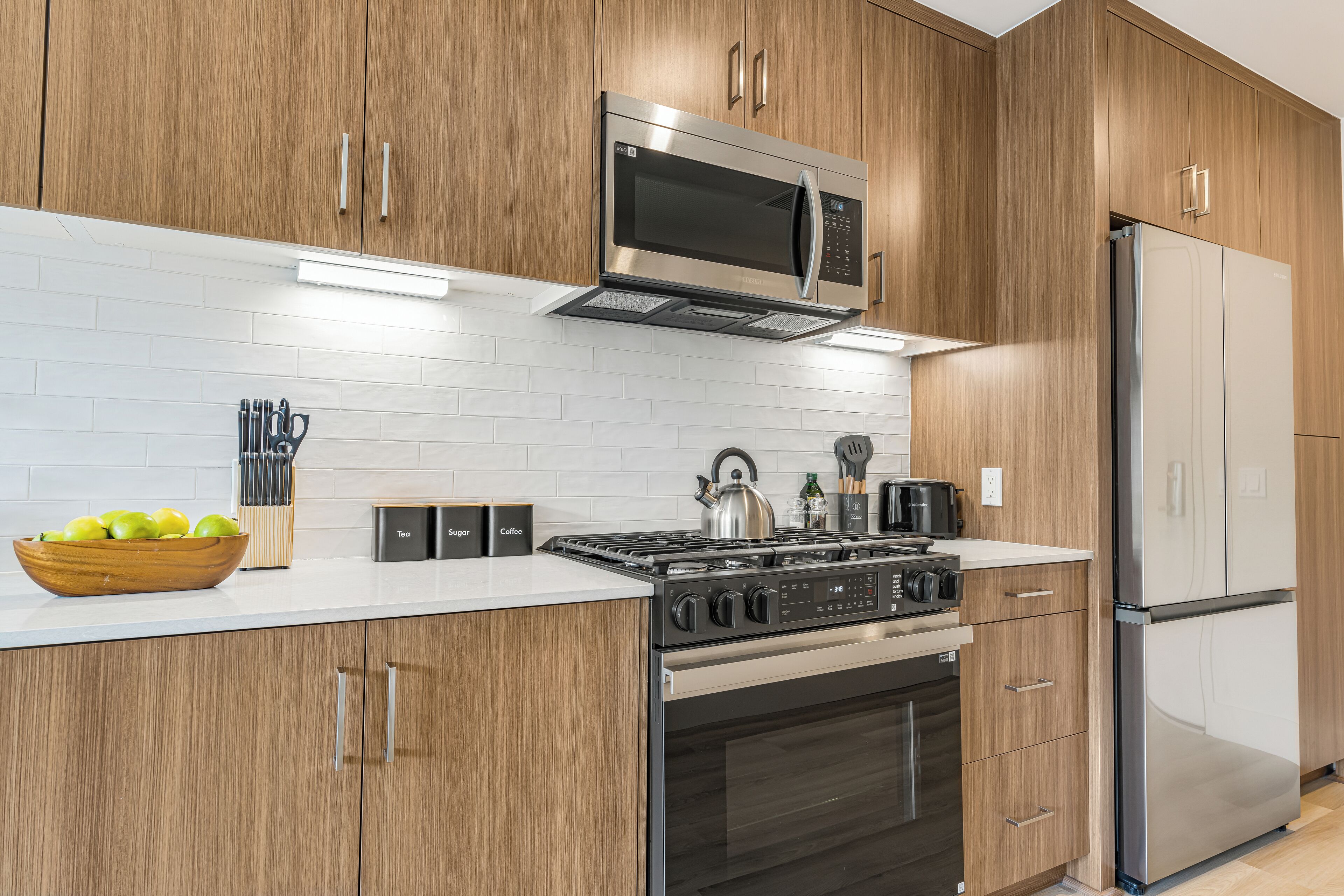A modern kitchen with wooden cabinets, a stainless steel microwave, a gas stove, and a refrigerator.