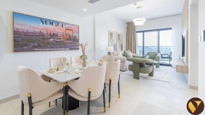 A modern hotel room with a dining area, a large window, and a cityscape view. - Vogue | Binghatti Creek near Festival City Mall (Dubai)
