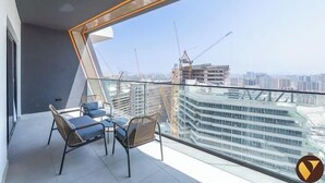 A balcony with two wicker chairs and a glass table, overlooking a cityscape with buildings and construction cranes. - Vogue | Binghatti Creek near Festival City Mall (Dubai)