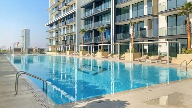 A modern hotel with a swimming pool, multiple balconies, and palm trees. - Vogue | Binghatti Creek near Festival City Mall (Dubai)