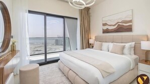 A modern hotel room with a large bed, a view of the city through floor-to-ceiling windows, a round mirror, and a contemporary light fixture. - Vogue | Binghatti Creek near Festival City Mall (Dubai)