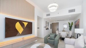 A modern living room with a large wall-mounted TV, a dining area with a table and chairs, and a sofa. - Vogue | Binghatti Creek near Festival City Mall (Dubai)