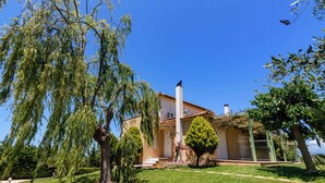 Ein Haus mit weißer Fassade, einem Ziegeldach und einem Garten mit Bäumen und Rasen.