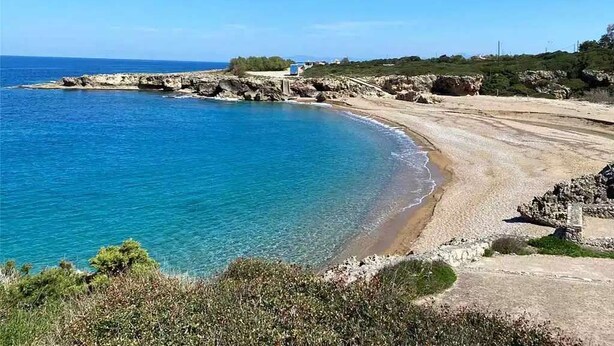 Eine Küstenlandschaft mit blauem Meer, felsiger Küste und einem Gebäude in der Ferne.
