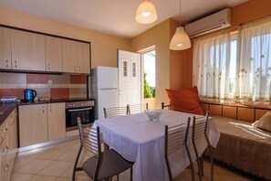 A compact kitchen with a dining area, a white table, and a sofa with a window view.