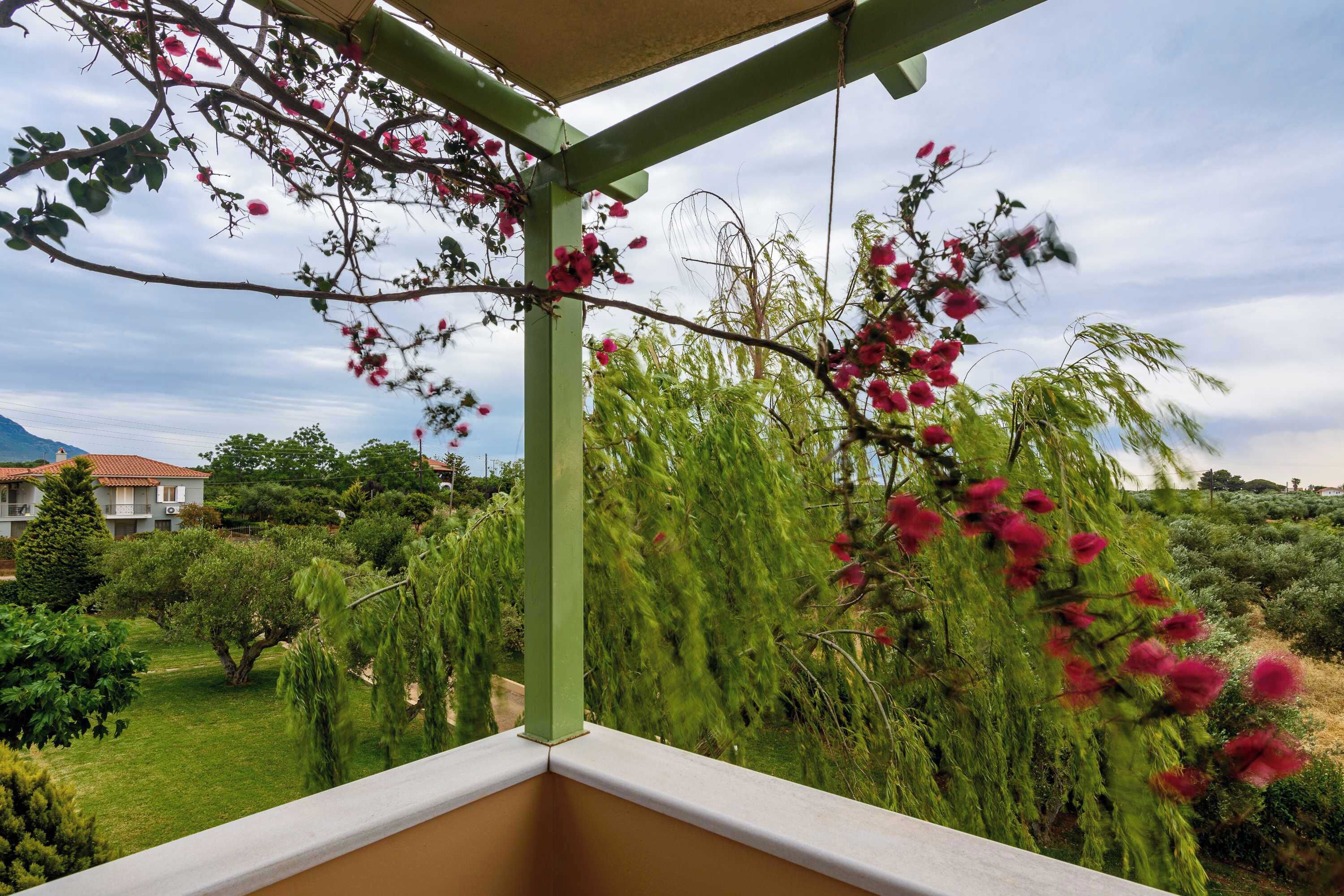 A balcony with a view of a garden, a house in the background, and a clear sky.