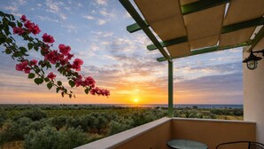 Ein Balkon mit Blick auf einen Sonnenuntergang über einer Wüstenlandschaft, ein Tisch und zwei Stühle.