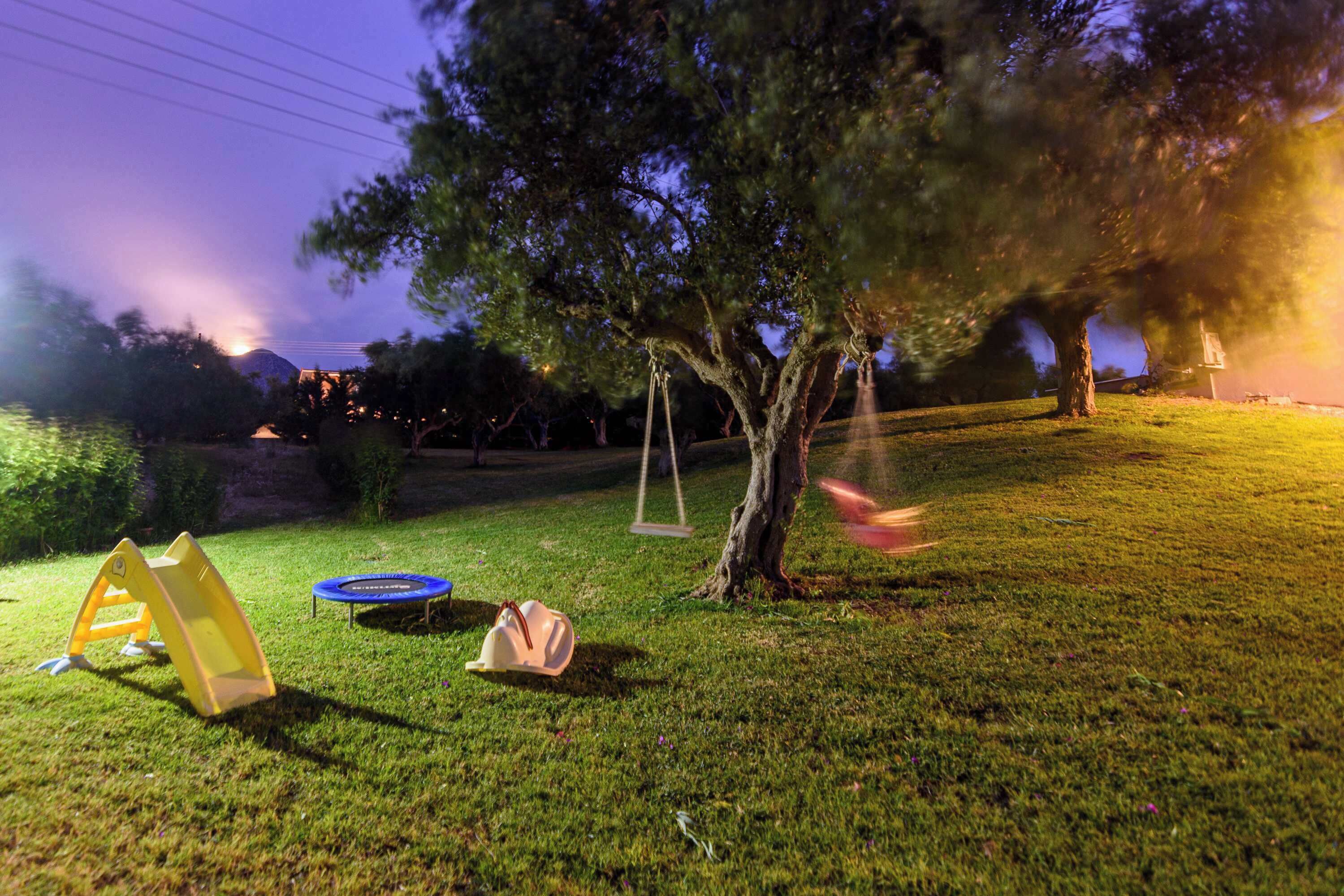 A grassy outdoor area with a swing set, a trampoline, and a tent.