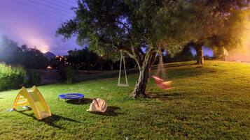 A grassy outdoor area with a swing set, a trampoline, and a tent.