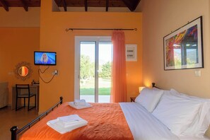 Habitación de hotel con cama, televisor, escritorio con silla y ventana con cortina.
