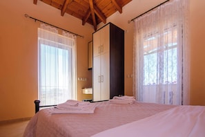 Une chambre à coucher avec un lit, une armoire et deux fenêtres ornées de rideaux légers.