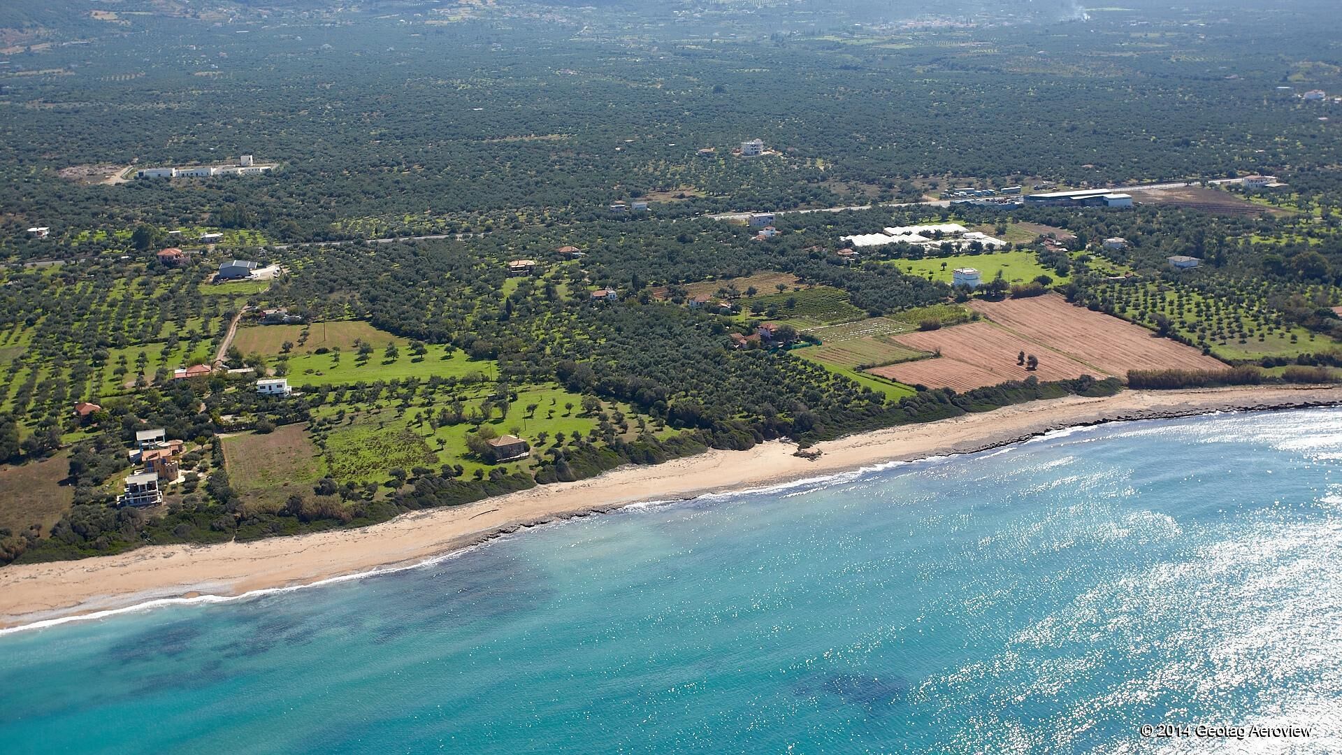 An aerial view of a coastal area with a beach, agricultural fields, and scattered buildings.