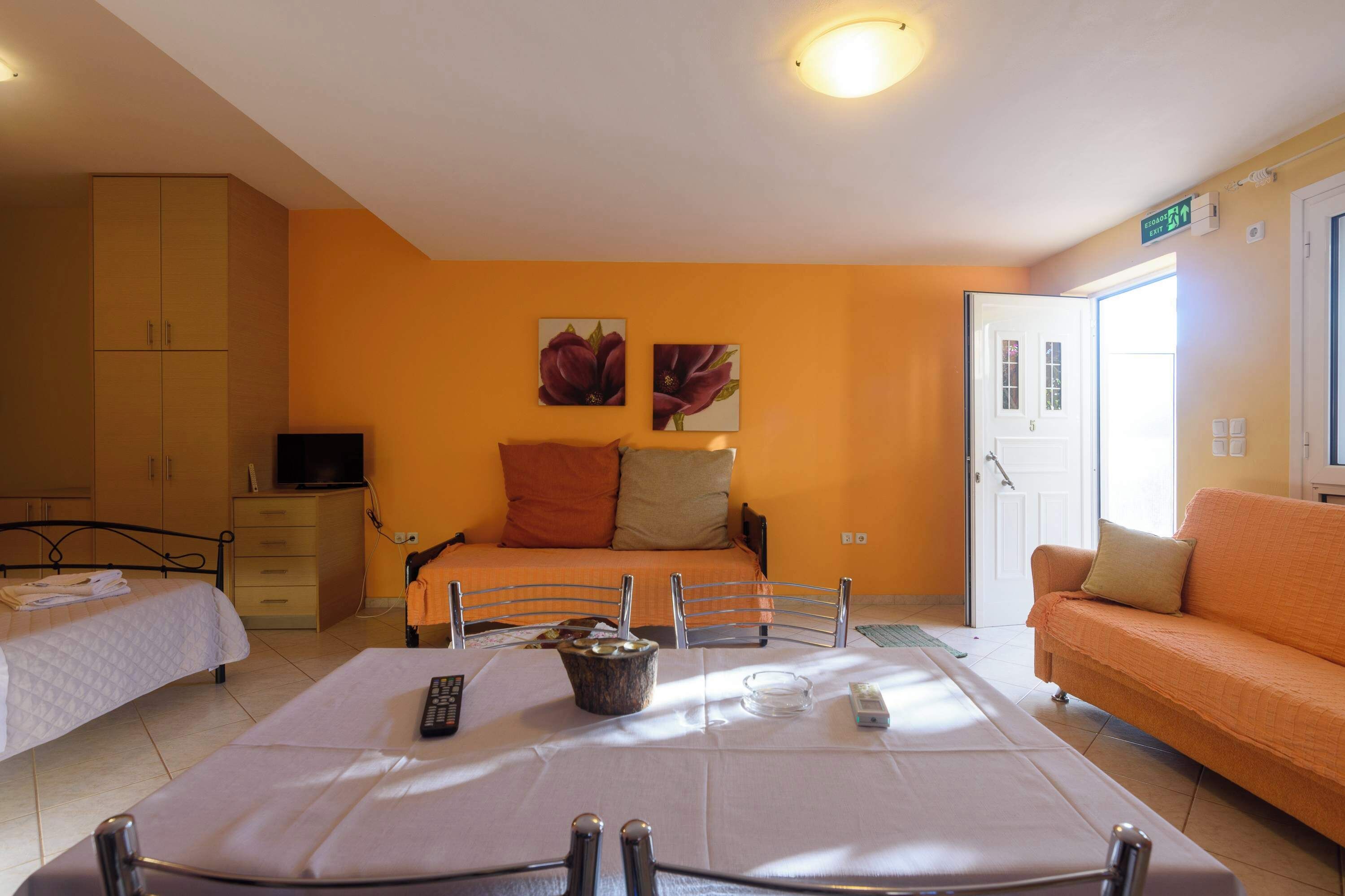 A hotel room with a bed, a sofa, a dining table, and a television.