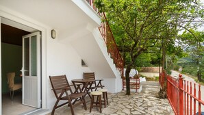 Un patio con suelo de piedra, una mesa con sillas, una barandilla roja y un árbol.