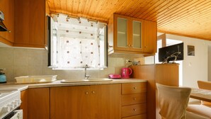 Una cocina con armarios de madera, una ventana con cortinas, un lavabo, una estufa y una silla.