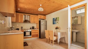 A kitchen with wooden cabinets, a stainless steel refrigerator, a dining table with chairs, and a bathroom with a sink and mirror. - Villa Liana Country House with Sea View (Φρίκες)