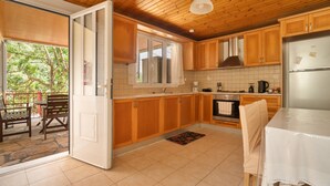 A kitchen with wooden cabinets, a stainless steel refrigerator, and a dining area with a table and chairs. - Villa Liana Country House with Sea View (Φρίκες)