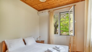A bedroom with a wooden ceiling, a bed with white linens, a nightstand with a lamp, and a window with curtains. - Villa Liana Country House with Sea View (Φρίκες)