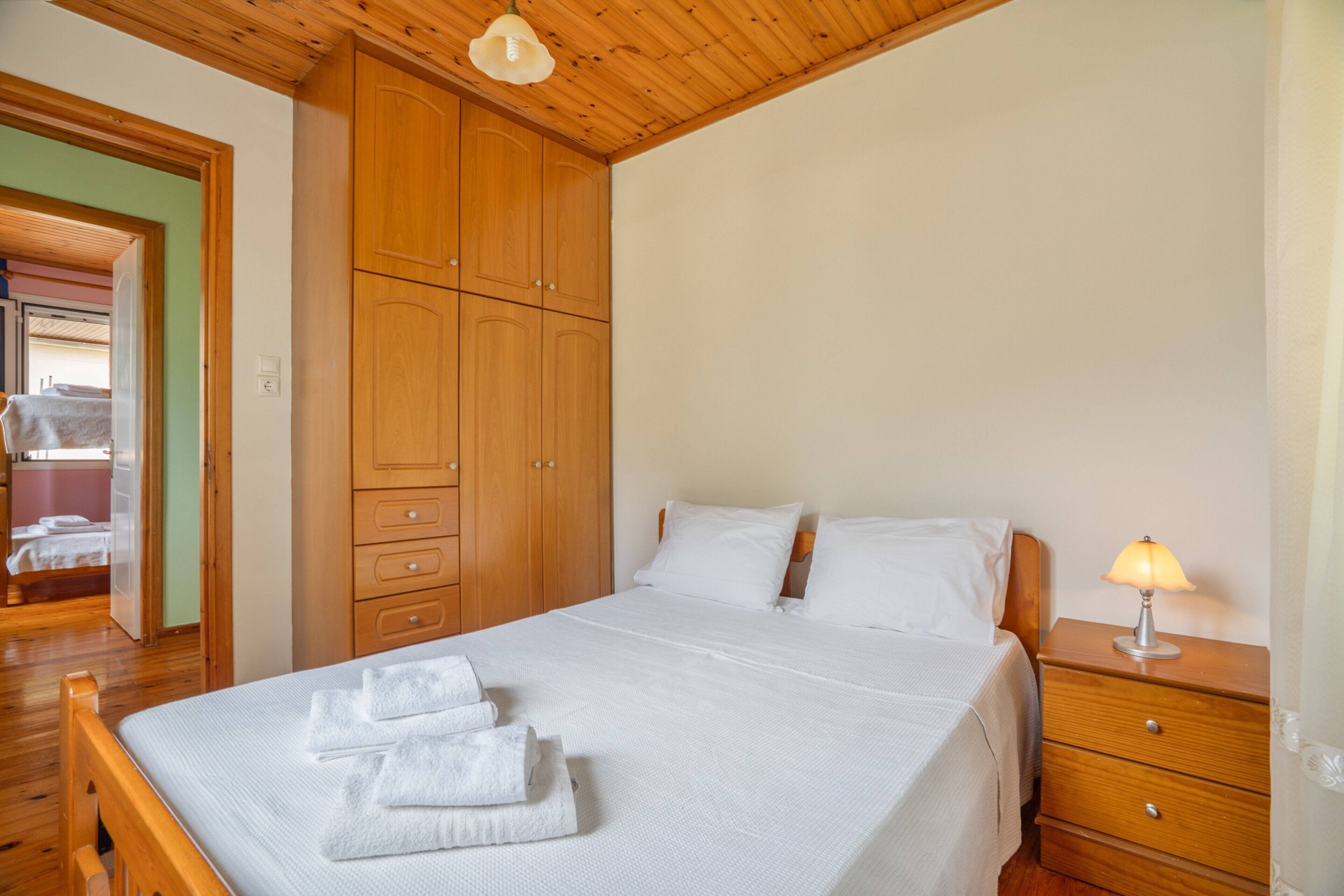 Een slaapkamer met een houten bed, een nachtkastje met een lamp en een houten garderobe.