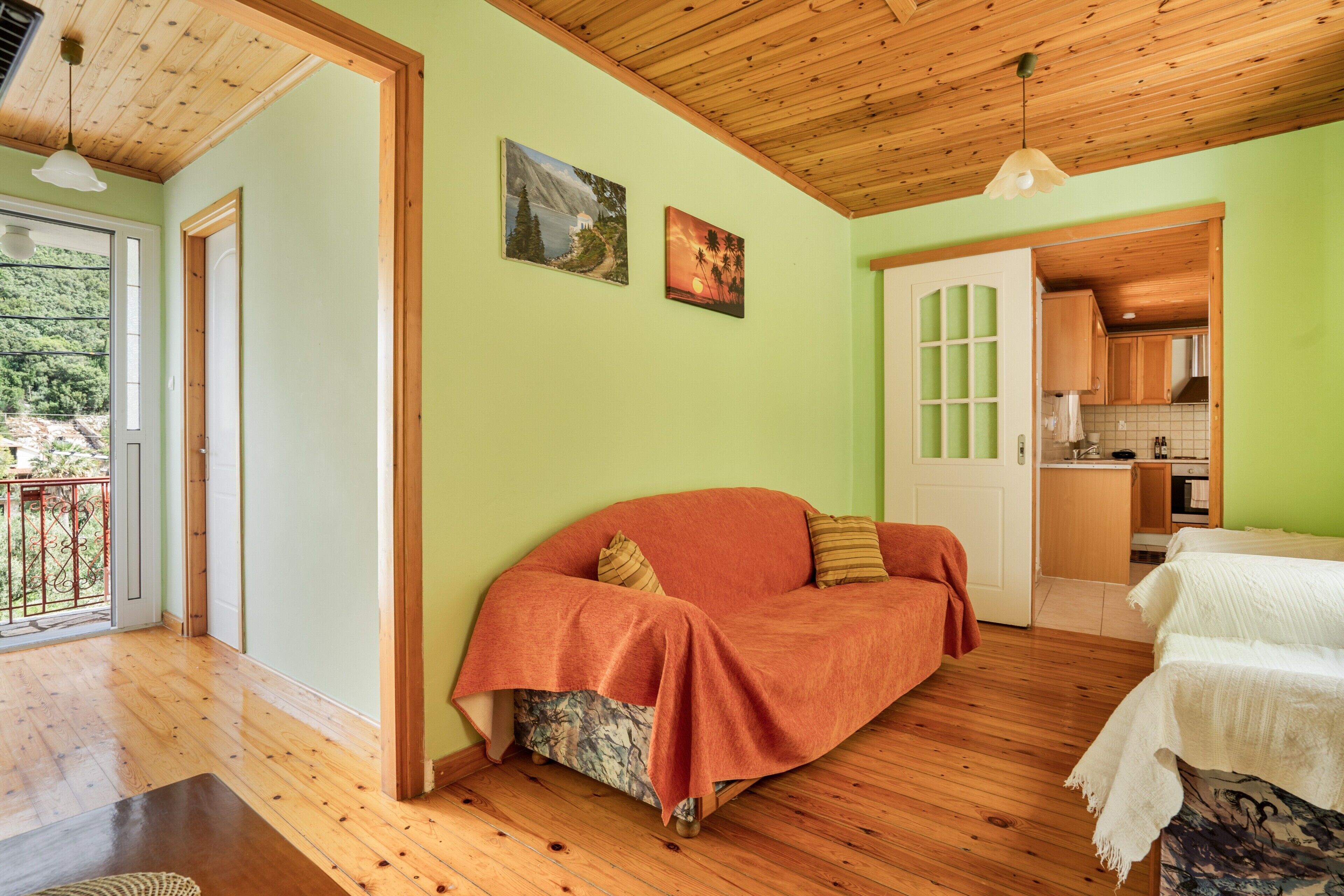 Ein Zimmer mit Holzboden, einer Couch, einem Bett, einer Küchenzeile und einer Tür, die auf einen Balkon führt.