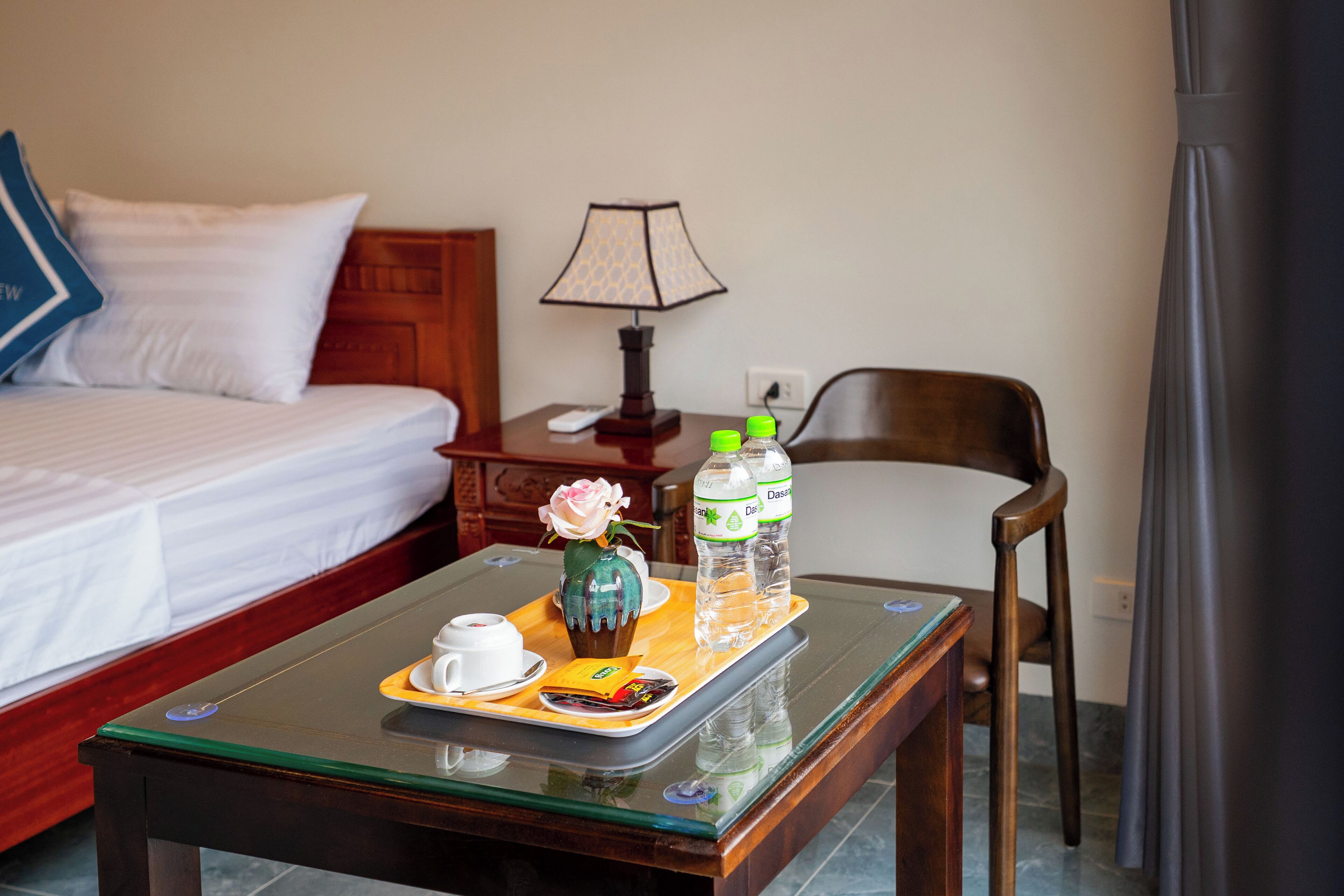 Una habitación de hotel con cama, mesita de noche, una mesa con una bandeja de desayuno, lámpara y una silla.