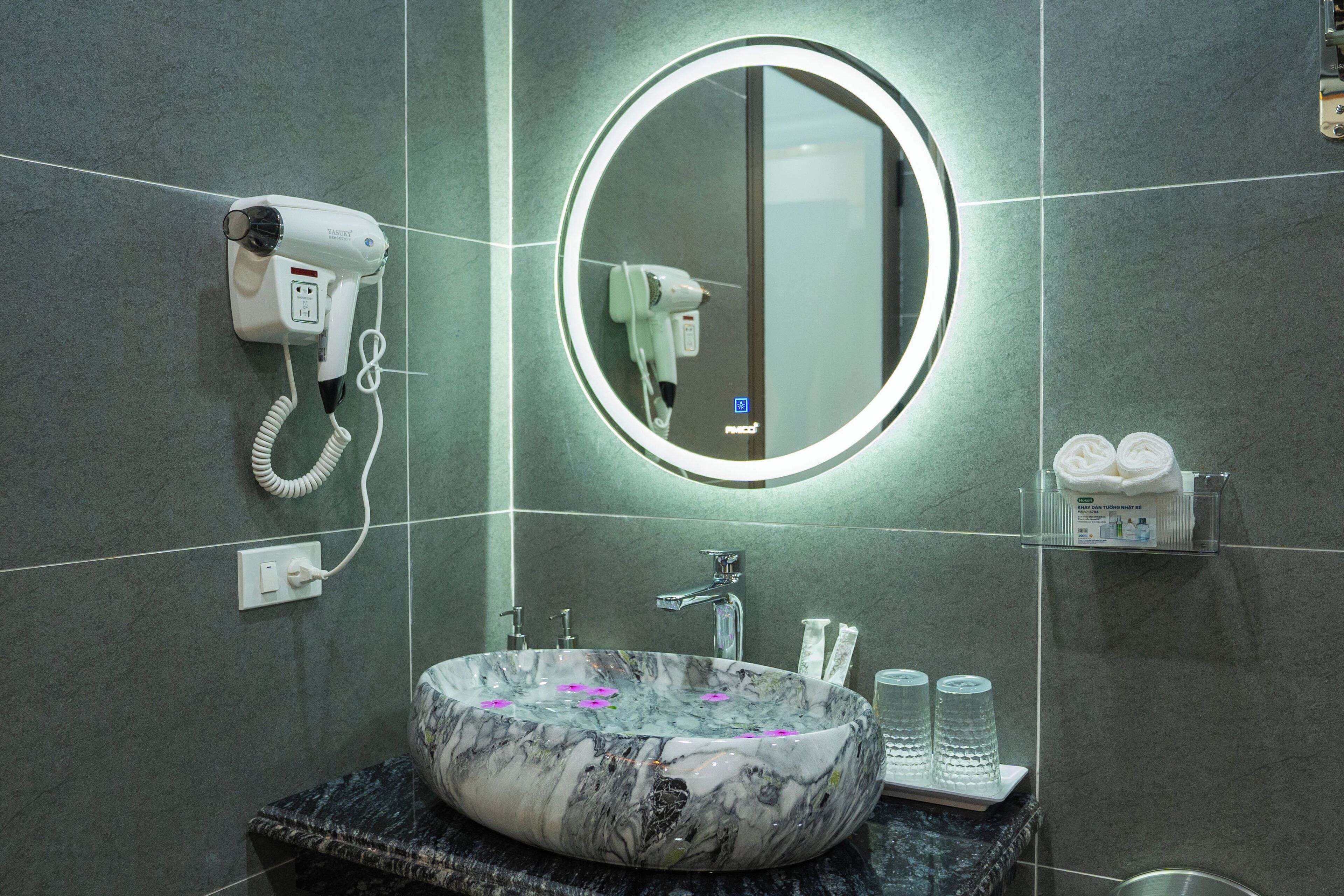 A bathroom with a marble sink, a round mirror, a hairdryer, and a towel rack.