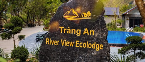 A large rock with 'Trang An River View Ecolodge' written on it, surrounded by greenery and a pool.