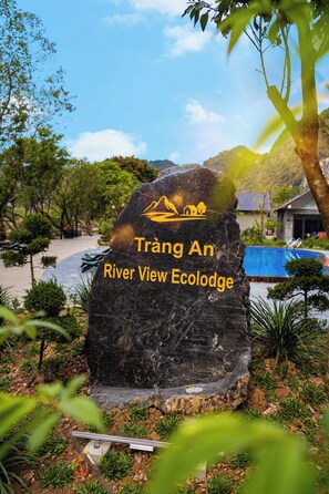 A large rock with 'Trang An River View Ecolodge' written on it, surrounded by greenery and a pool. - Trang An River View Ecolodge (Tay Hoa Lu)