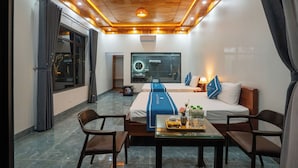 A hotel room with a wooden ceiling, a bed with a blue bedspread, a desk with a tray of items, and a view of the outside.