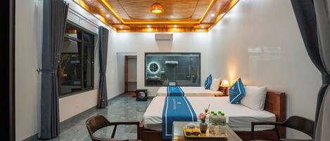 A hotel room with a wooden ceiling, a bed with a blue bedspread, a desk with a tray of items, and a view of the outside.