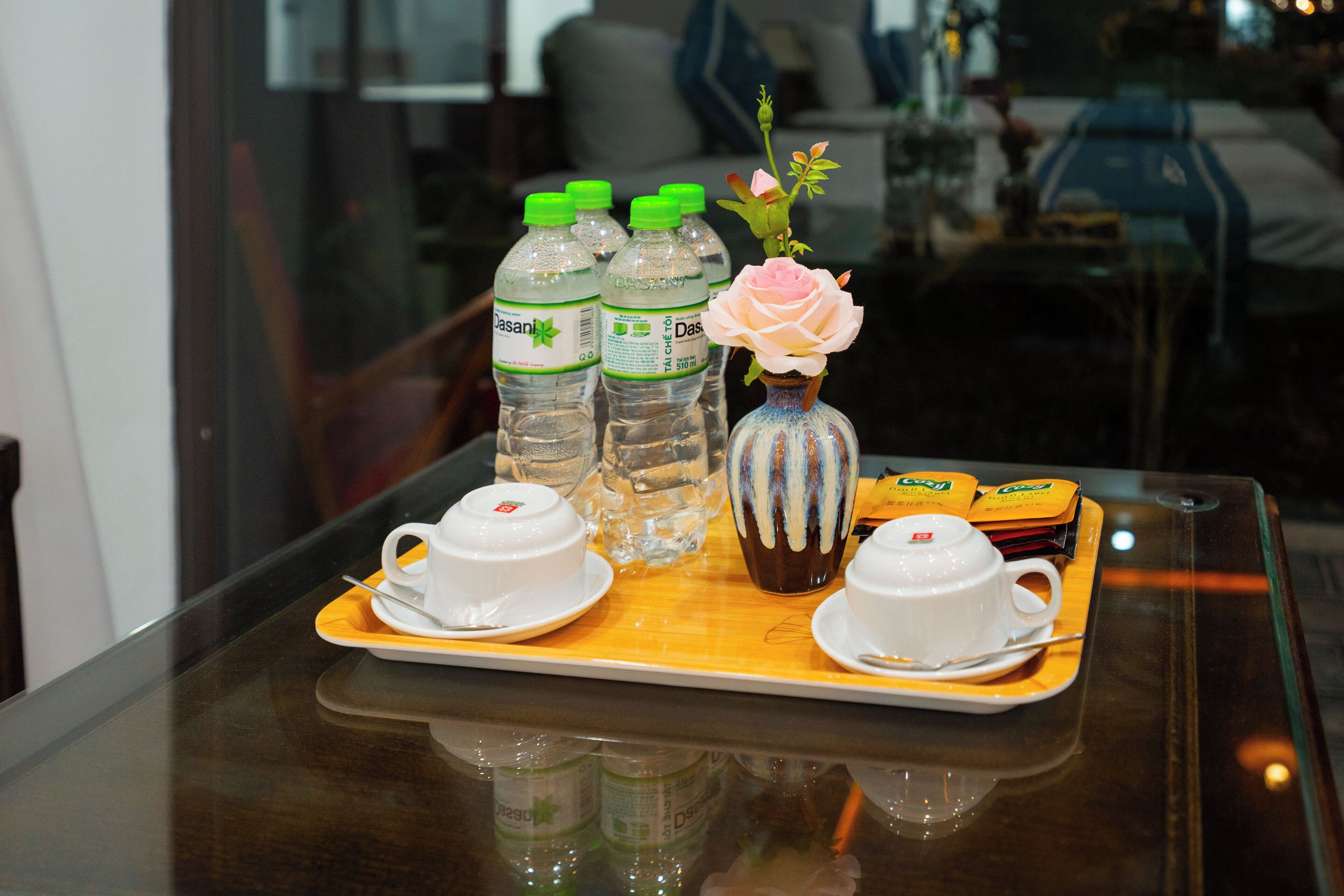 A tray with water bottles, a vase with a flower, and tea packets on a reflective surface.