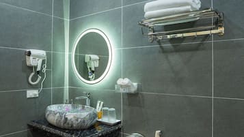 Een badkamer met een marmeren wastafel, een ronde spiegel met verlichting, een haardroger, een handdoekhouder en een zeepdispenser.