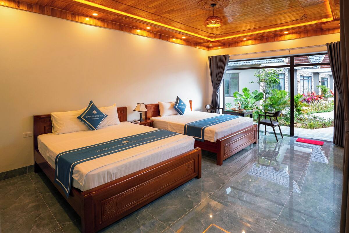 A hotel room with two wooden beds, a small table, a chair, and a view of the outside.