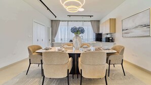 Un comedor moderno con una mesa redonda, cuatro sillas, un jarrón con flores y una lámpara de diseño contemporáneo.