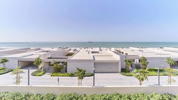 Un moderno complejo residencial con varias edificaciones, vista despejada al mar y un paseo pavimentado con áreas verdes.