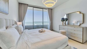 Un dormitorio moderno con una cama grande, un aparador, un espejo y vista al océano.