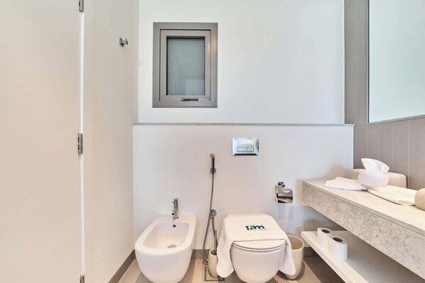 Une salle de bain moderne équipée d’un bidet, de toilettes et d’une petite fenêtre.